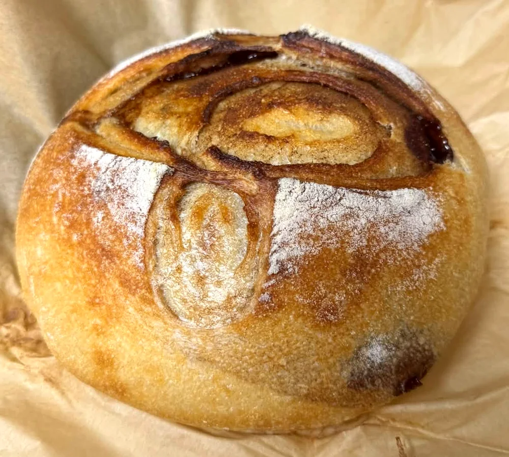 A cinnamon swirl sourdough loaf with a golden, floured crust